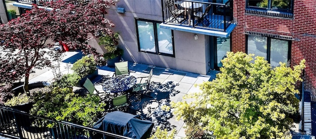 exterior space with brick siding, a patio area, and a balcony