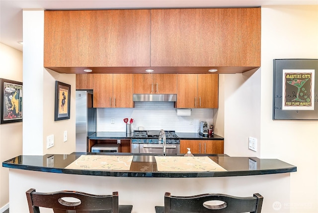 kitchen with range hood, brown cabinetry, a peninsula, a kitchen breakfast bar, and tasteful backsplash