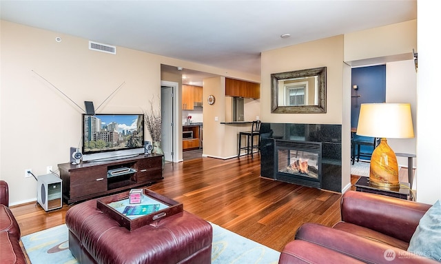 living area with a fireplace, wood finished floors, visible vents, and baseboards