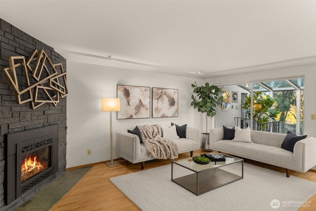 living room featuring baseboards, a brick fireplace, wood finished floors, and a sunroom