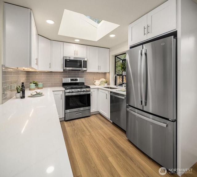 kitchen with light wood-style flooring, a skylight, a sink, stainless steel appliances, and light countertops