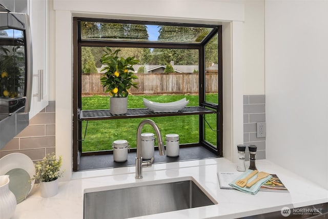 interior details with a sink, decorative backsplash, and light stone countertops