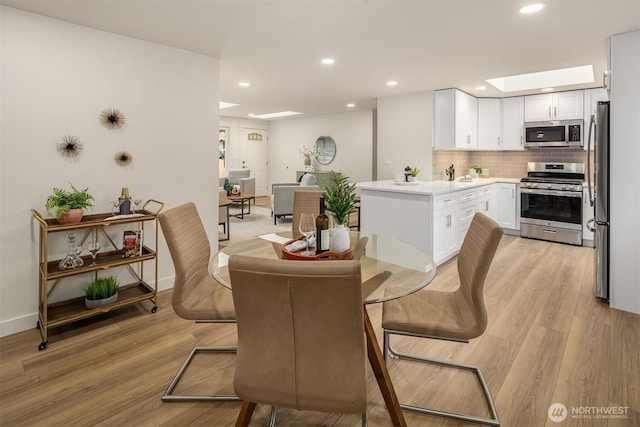 dining space with a skylight, recessed lighting, light wood-style flooring, and baseboards