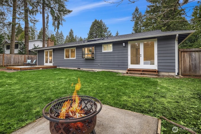 back of property featuring fence, a chimney, french doors, a deck, and a lawn