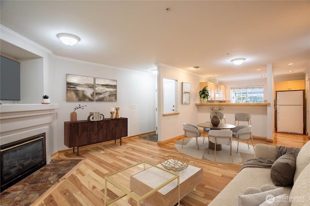 living area featuring a glass covered fireplace, crown molding, baseboards, and wood finished floors