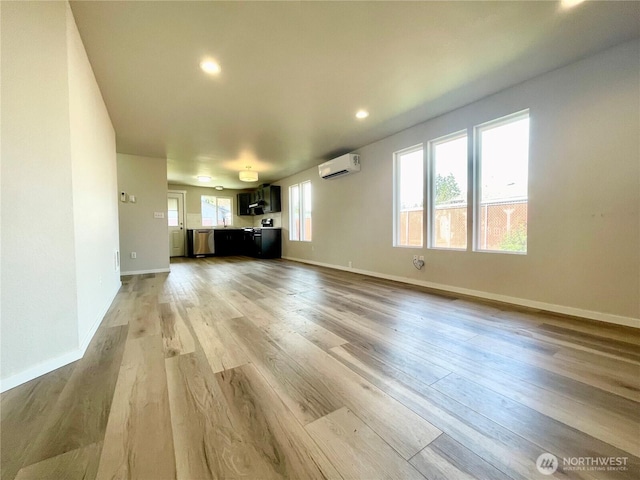 unfurnished living room with a wall unit AC, recessed lighting, a sink, light wood-type flooring, and baseboards