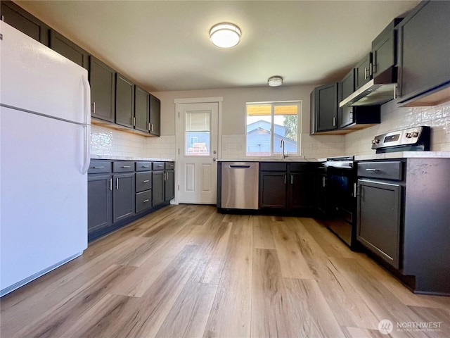 kitchen with tasteful backsplash, light countertops, appliances with stainless steel finishes, light wood-type flooring, and under cabinet range hood