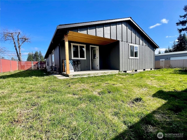 rear view of property featuring a lawn, a patio, crawl space, fence, and board and batten siding