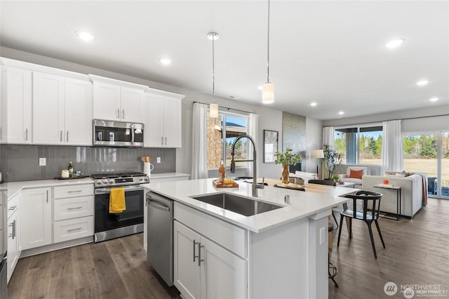 kitchen with a center island with sink, decorative backsplash, dark wood-style flooring, stainless steel appliances, and a sink