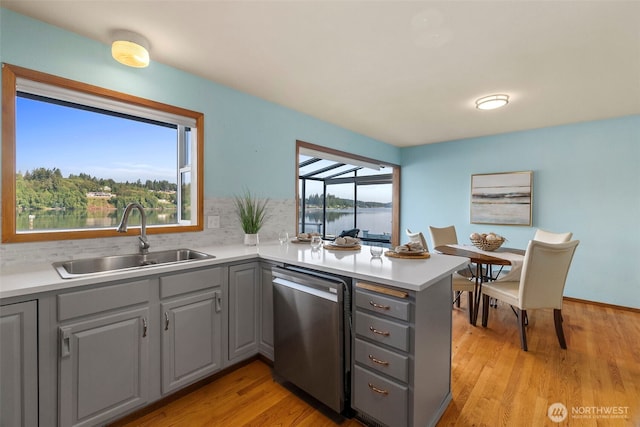 kitchen with light wood finished floors, a peninsula, a sink, gray cabinetry, and dishwasher