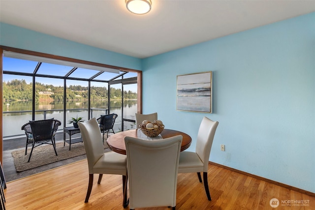 dining area featuring baseboards, a water view, light wood-style flooring, and a sunroom