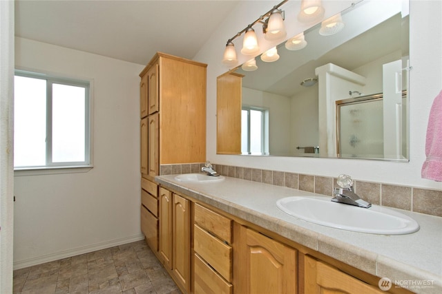 full bathroom featuring double vanity, a stall shower, baseboards, and a sink