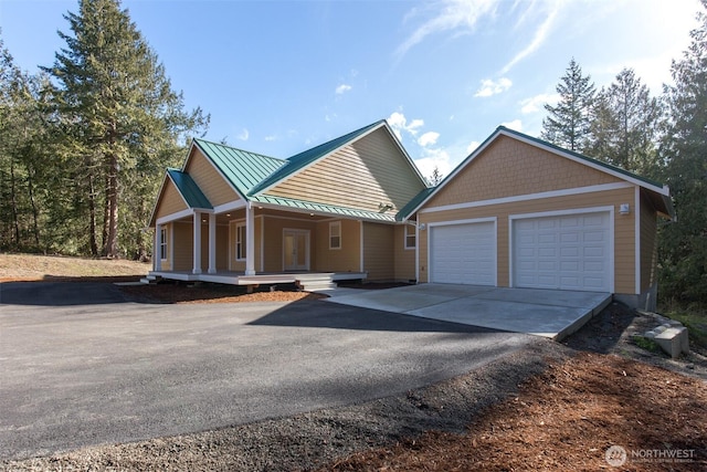 view of front facade with driveway, a garage, metal roof, a standing seam roof, and a porch