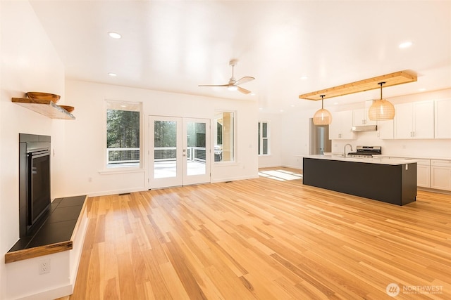 unfurnished living room featuring recessed lighting, baseboards, french doors, light wood finished floors, and a glass covered fireplace