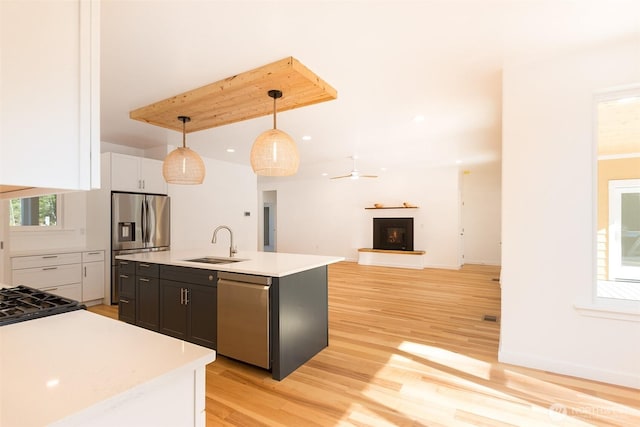 kitchen featuring light wood finished floors, light countertops, appliances with stainless steel finishes, a sink, and a warm lit fireplace