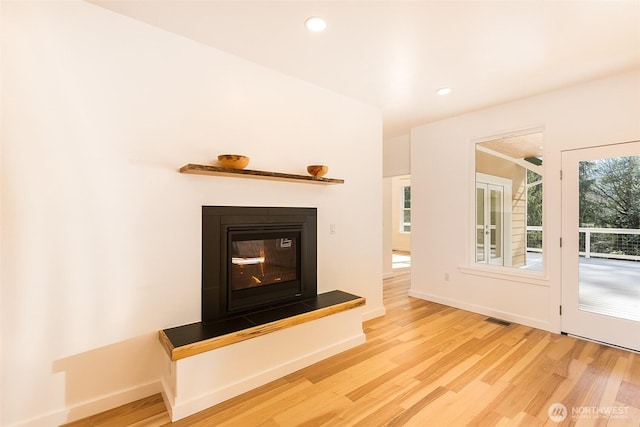 unfurnished living room featuring light wood-type flooring, baseboards, visible vents, and a glass covered fireplace