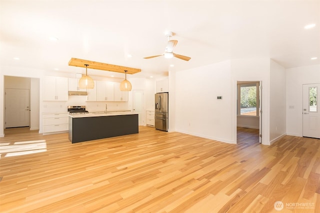 kitchen featuring light wood-style flooring, under cabinet range hood, a sink, white cabinetry, and appliances with stainless steel finishes