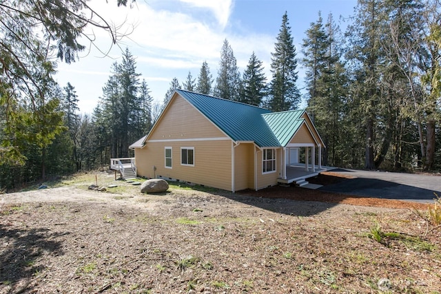 view of side of home with crawl space, metal roof, a view of trees, and a standing seam roof