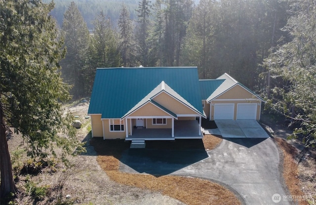 view of front of house with a garage, driveway, a forest view, metal roof, and a porch