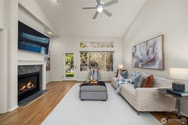 living room featuring high vaulted ceiling, a premium fireplace, baseboards, and wood finished floors