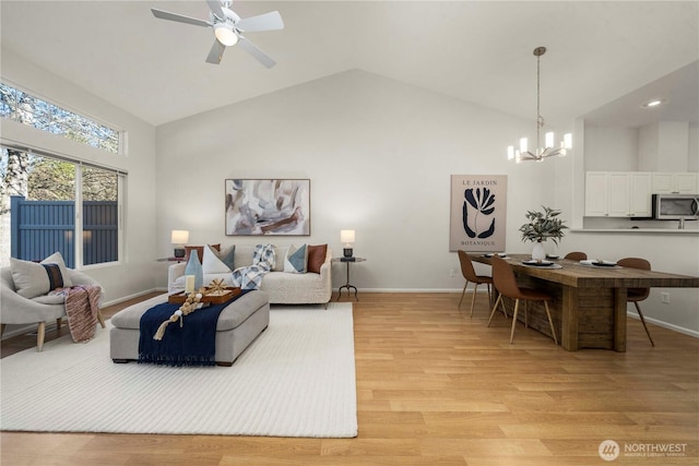 living room featuring ceiling fan with notable chandelier, high vaulted ceiling, light wood-style flooring, and baseboards