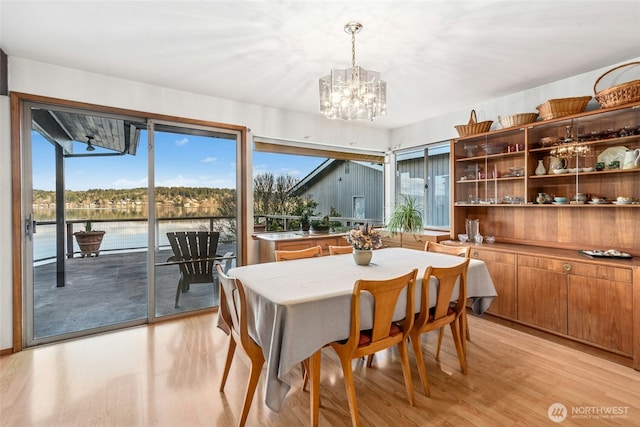 dining space featuring light wood-style flooring, a water view, and a chandelier