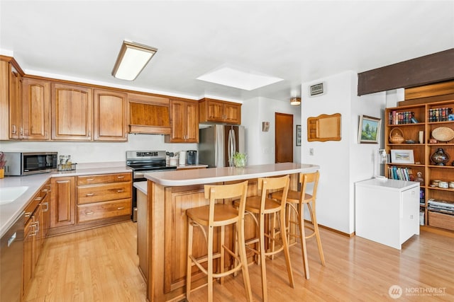 kitchen featuring a breakfast bar, stainless steel appliances, light countertops, light wood-type flooring, and a center island