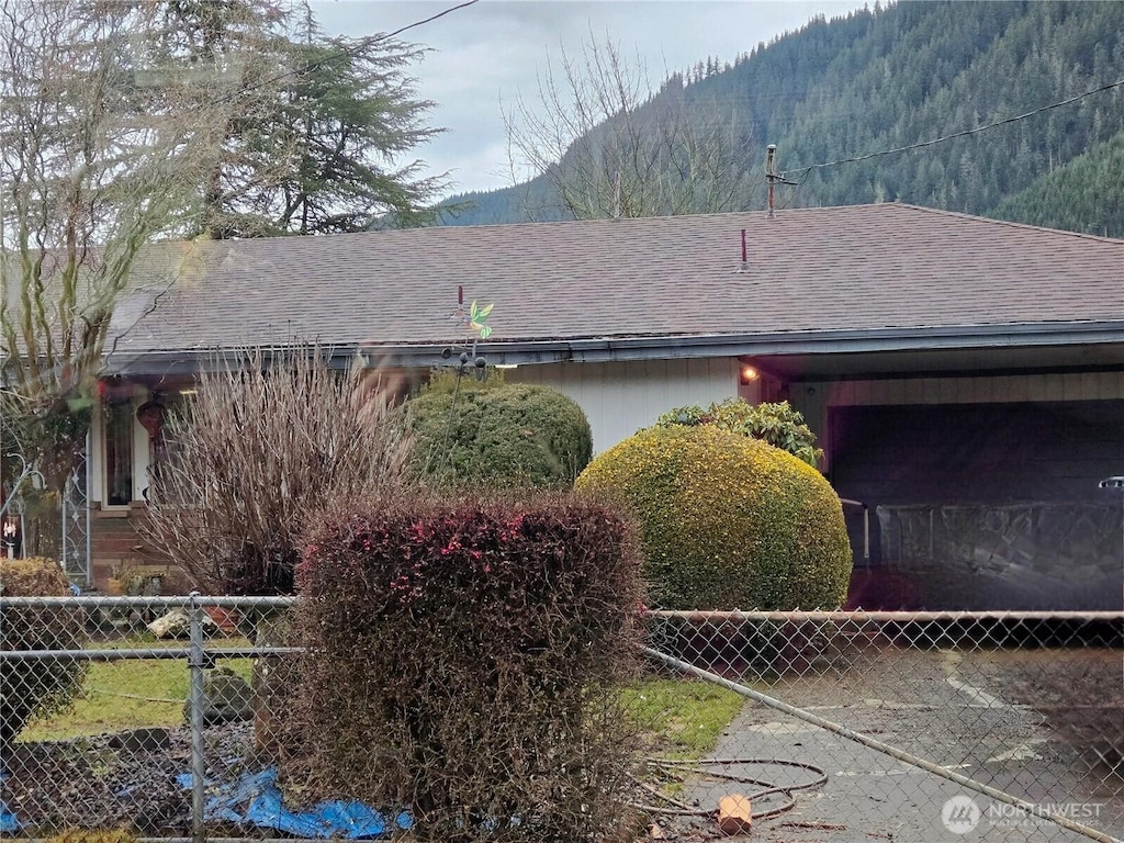 view of home's exterior with fence, a mountain view, and roof with shingles