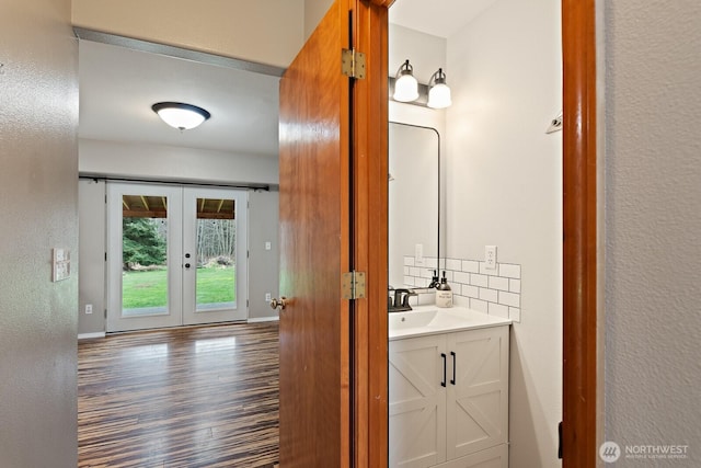 bathroom featuring wood finished floors, french doors, decorative backsplash, baseboards, and vanity