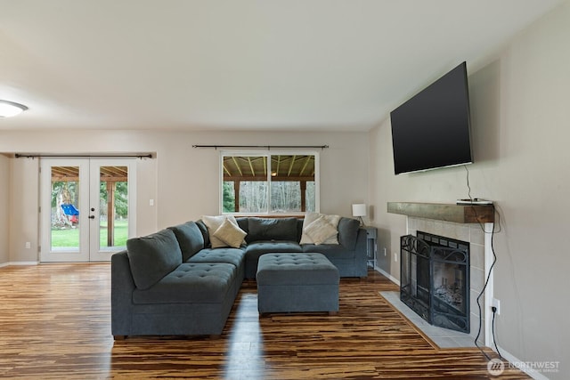 living room featuring a tiled fireplace, a healthy amount of sunlight, french doors, and wood finished floors