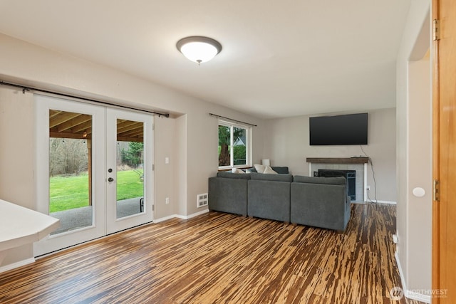 living room featuring visible vents, dark wood finished floors, french doors, baseboards, and a tile fireplace