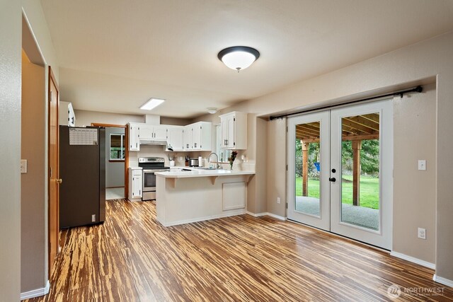 kitchen with light countertops, appliances with stainless steel finishes, french doors, a peninsula, and light wood-style floors