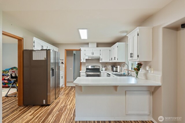 kitchen featuring a peninsula, a sink, stainless steel appliances, light countertops, and white cabinetry