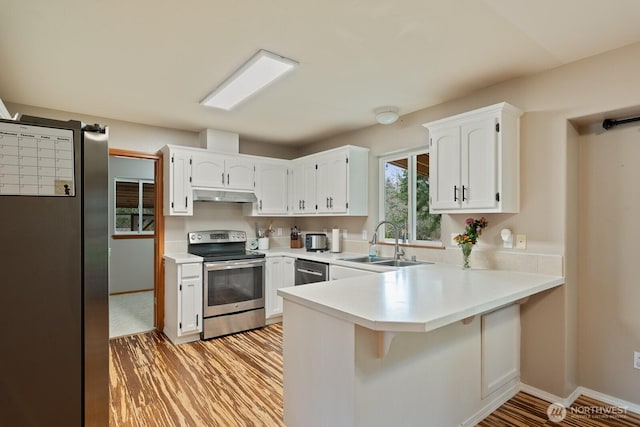 kitchen with under cabinet range hood, a sink, stainless steel appliances, a peninsula, and light wood finished floors