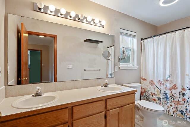 full bath with double vanity, curtained shower, toilet, and a sink