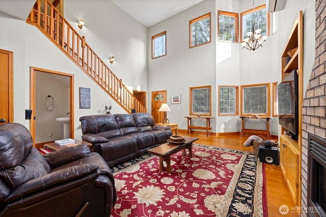 living room featuring stairway, wood finished floors, an inviting chandelier, a towering ceiling, and a brick fireplace