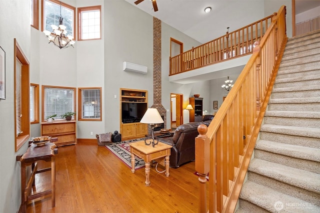 living area featuring stairway, ceiling fan with notable chandelier, a high ceiling, hardwood / wood-style flooring, and a wall mounted AC