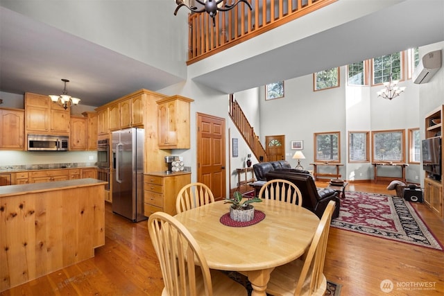 dining space featuring a wall mounted AC, plenty of natural light, wood finished floors, stairway, and a chandelier