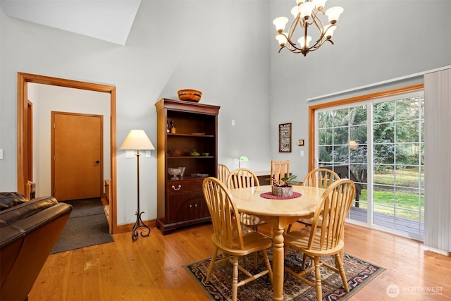 dining space with a notable chandelier, a healthy amount of sunlight, light wood-type flooring, and a high ceiling