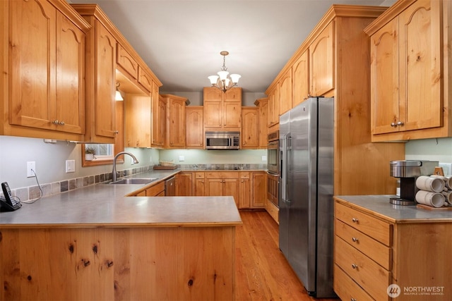 kitchen featuring light wood-type flooring, a sink, appliances with stainless steel finishes, a peninsula, and hanging light fixtures