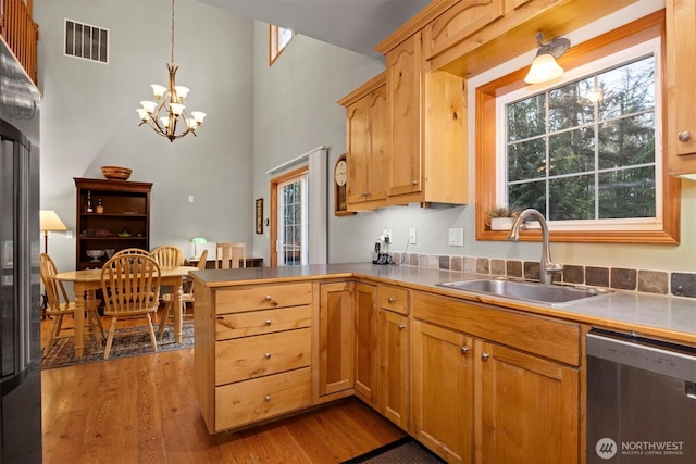 kitchen featuring visible vents, dishwasher, a peninsula, wood finished floors, and a sink