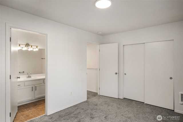 unfurnished bedroom featuring a closet, carpet flooring, connected bathroom, a sink, and baseboards