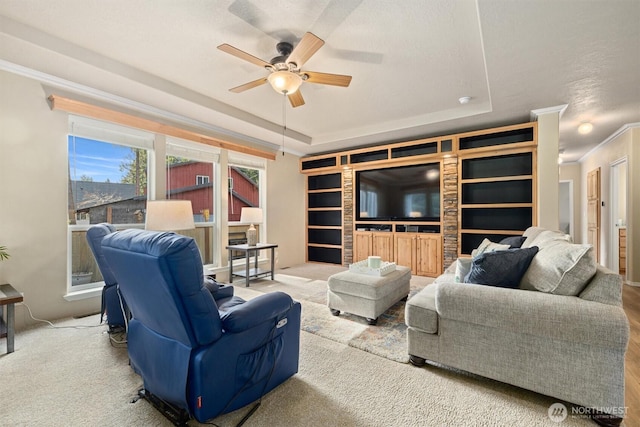 living area featuring built in features, a raised ceiling, a ceiling fan, and crown molding