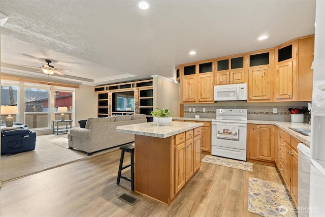 kitchen featuring a kitchen breakfast bar, open floor plan, a center island, white appliances, and light countertops