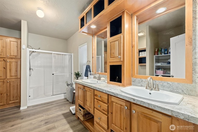 full bathroom with double vanity, a shower stall, wood finished floors, and a sink