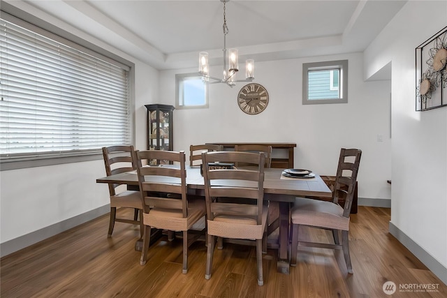 dining room featuring a chandelier, a raised ceiling, wood finished floors, and baseboards