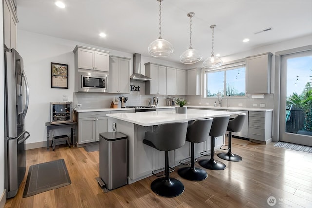 kitchen with wall chimney range hood, light wood-type flooring, appliances with stainless steel finishes, and gray cabinetry