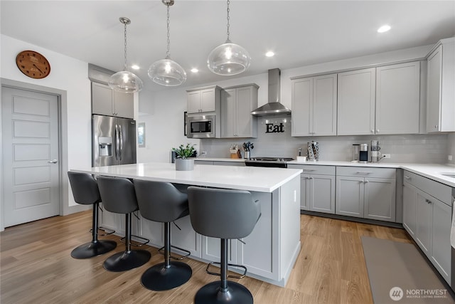 kitchen featuring wall chimney exhaust hood, a kitchen island, a breakfast bar area, stainless steel appliances, and gray cabinetry