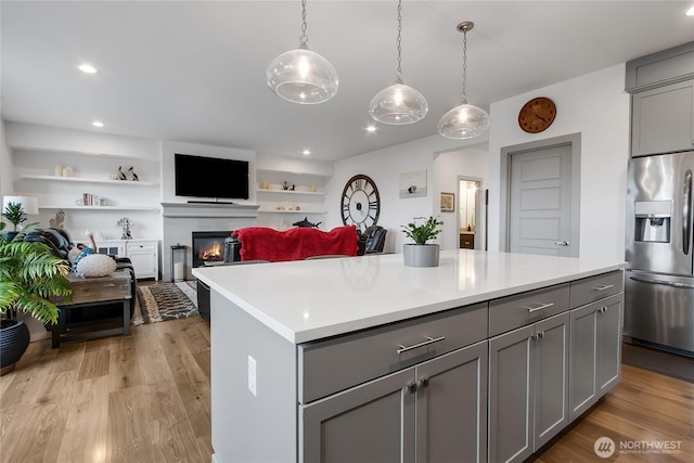 kitchen with light wood finished floors, a tiled fireplace, gray cabinets, light countertops, and stainless steel refrigerator with ice dispenser