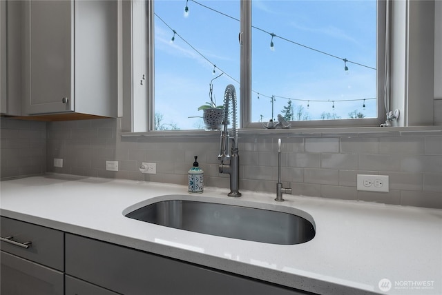 kitchen featuring light countertops, backsplash, a sink, and gray cabinetry